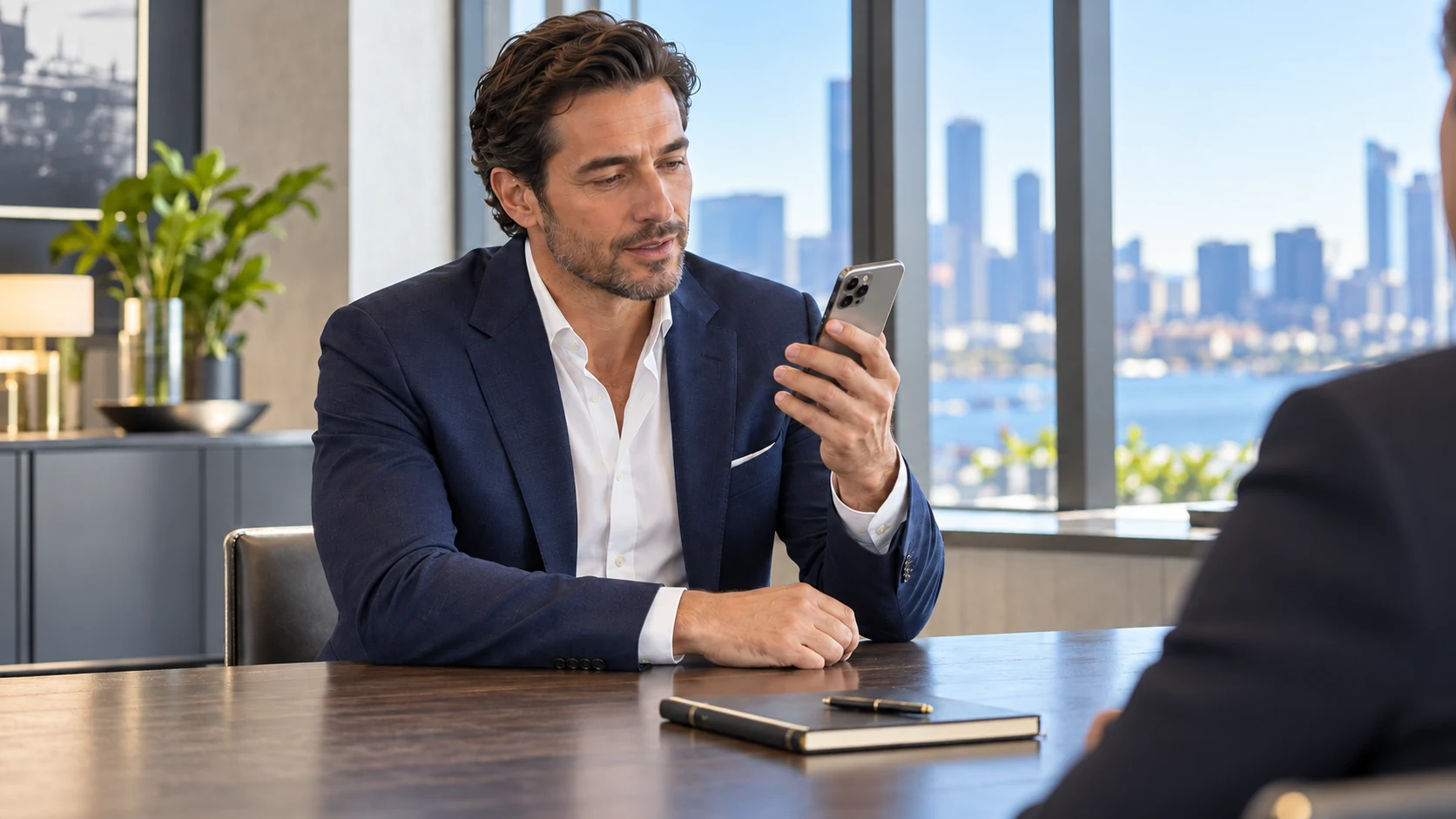 A man in a suit checks his iPhone at a desk during a conversation with the person opposite him.